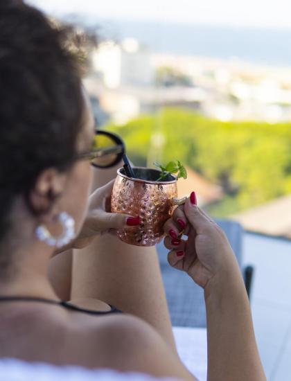 Donna con occhiali beve da una tazza di rame all'aperto.