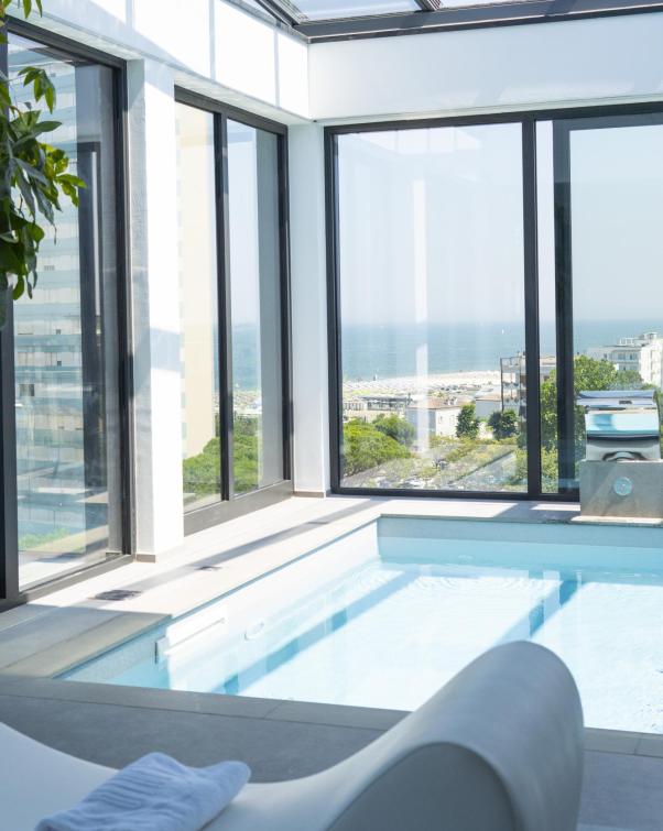 Piscina interna luminosa con vista mare attraverso ampie vetrate.