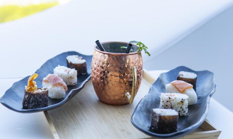 Sushi e cocktail su un vassoio con vista mare.