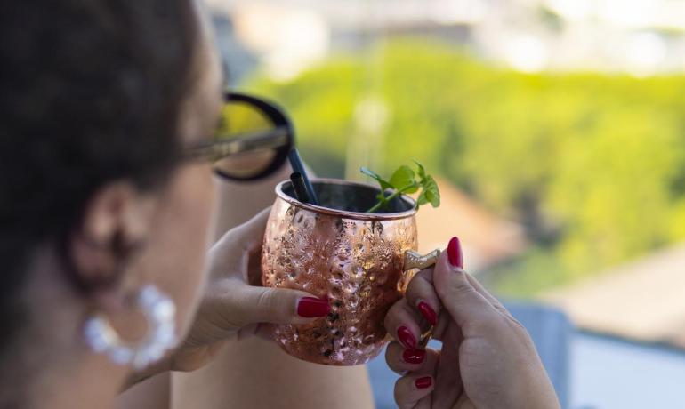 Donna con occhiali beve da una tazza di rame all'aperto.