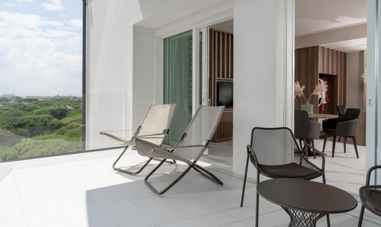 Terrazza luminosa con sedie moderne, vista su alberi e cielo sereno.