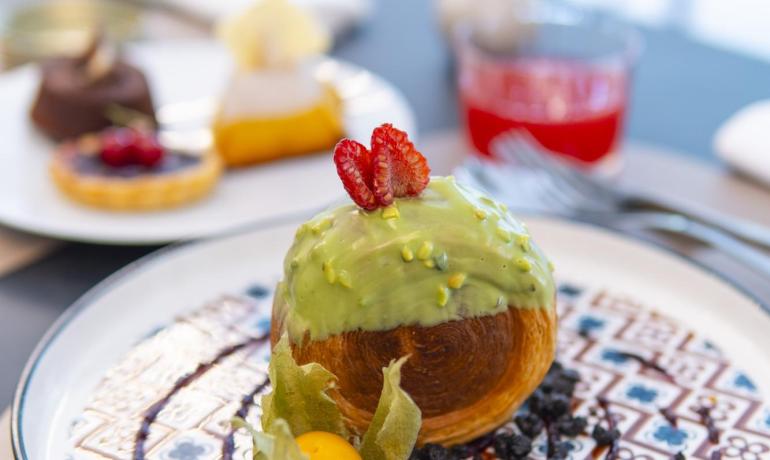 Dolce raffinato con glassa verde, fragola e decorazioni eleganti su piatto artistico.