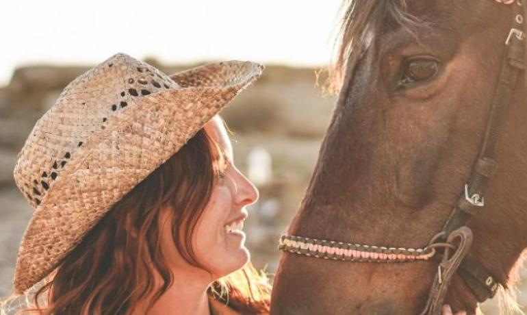 Donna sorridente accarezza un cavallo al tramonto, creando un momento di dolce connessione.