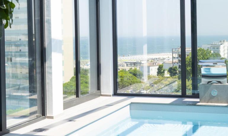 Piscina interna luminosa con vista mare attraverso ampie vetrate.