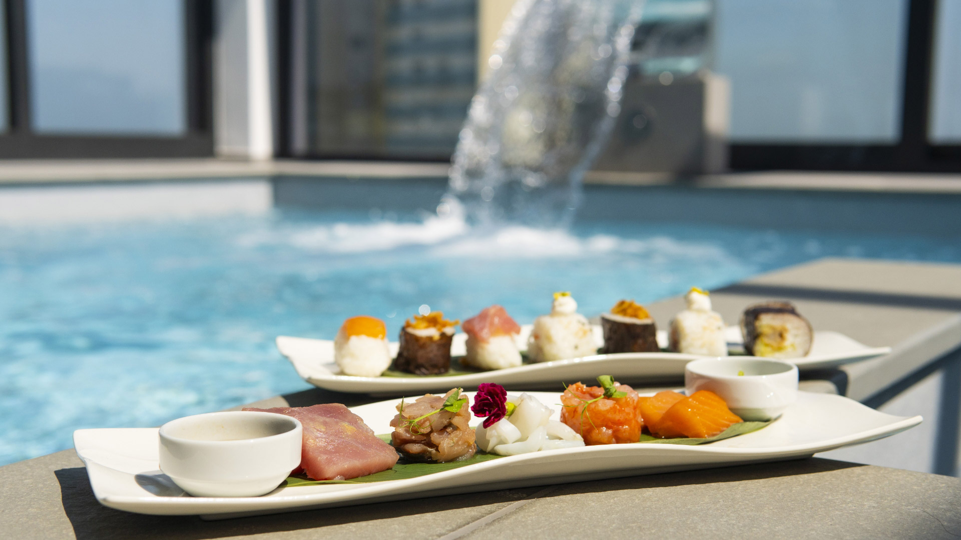 Sushi elegante e colorato su piatti raffinati, accanto a una piscina scintillante.