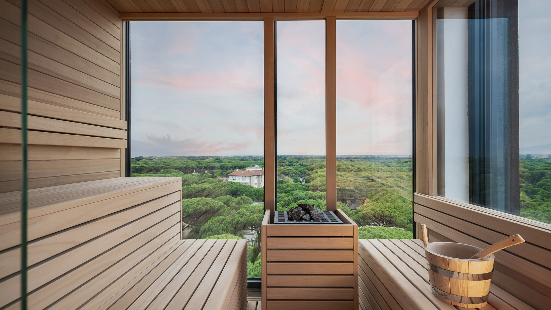 Sauna in legno con vista mozzafiato su foresta verde e cielo al tramonto.