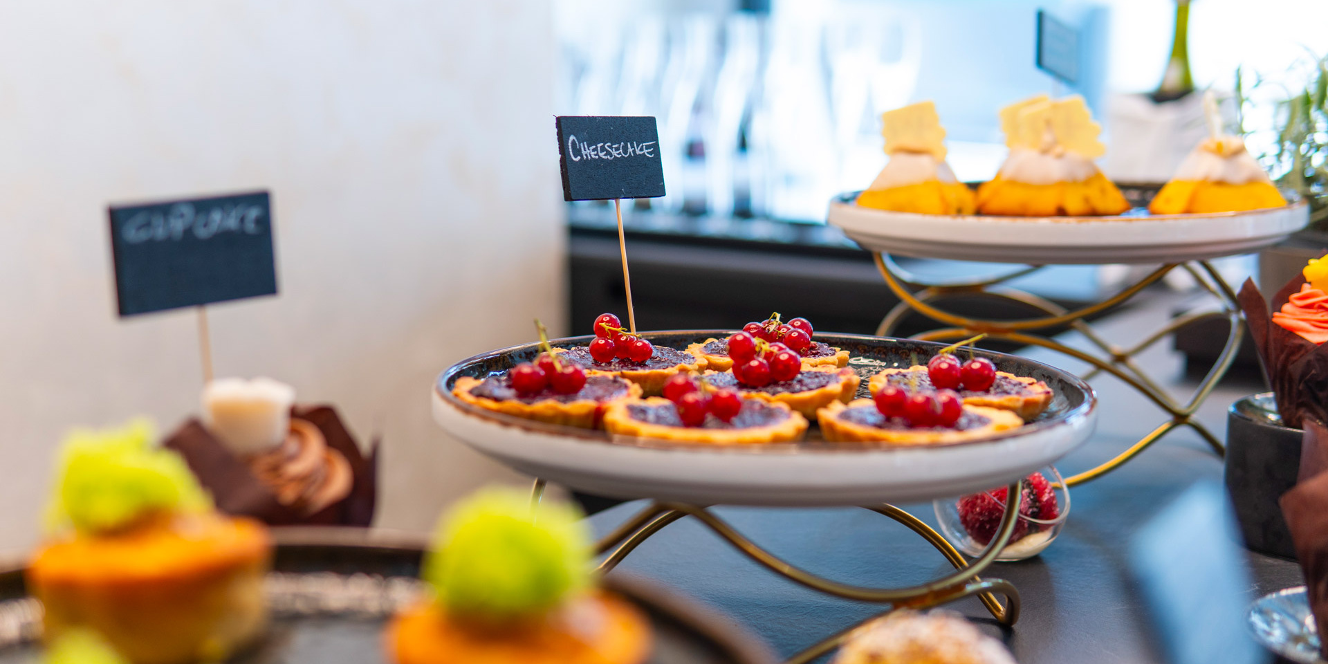 Dolci colorati su alzate eleganti, con etichette: cheesecake con frutti rossi, cupcake.