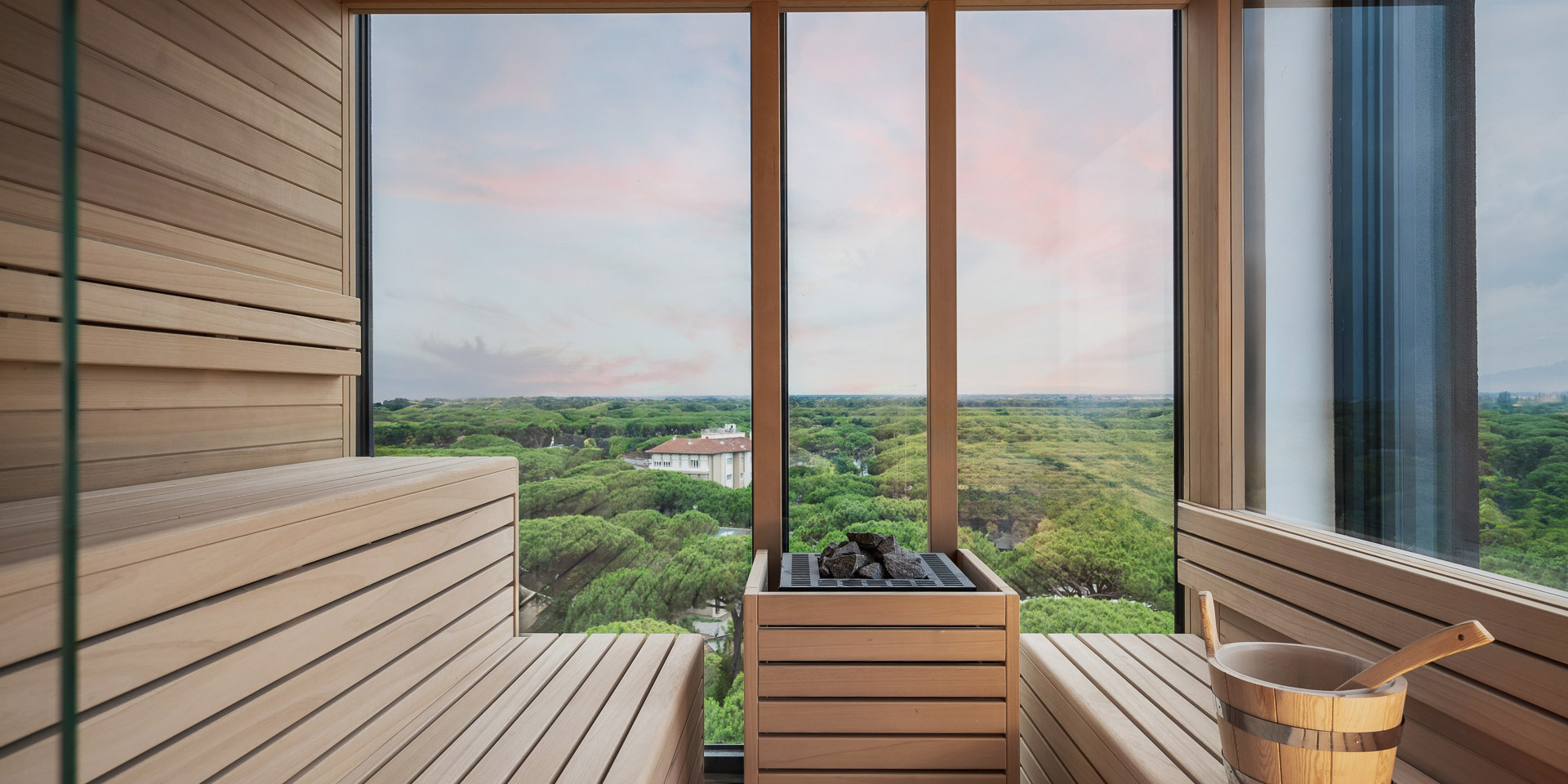 Sauna con vista panoramica su foresta verde, atmosfera rilassante e serena al tramonto.