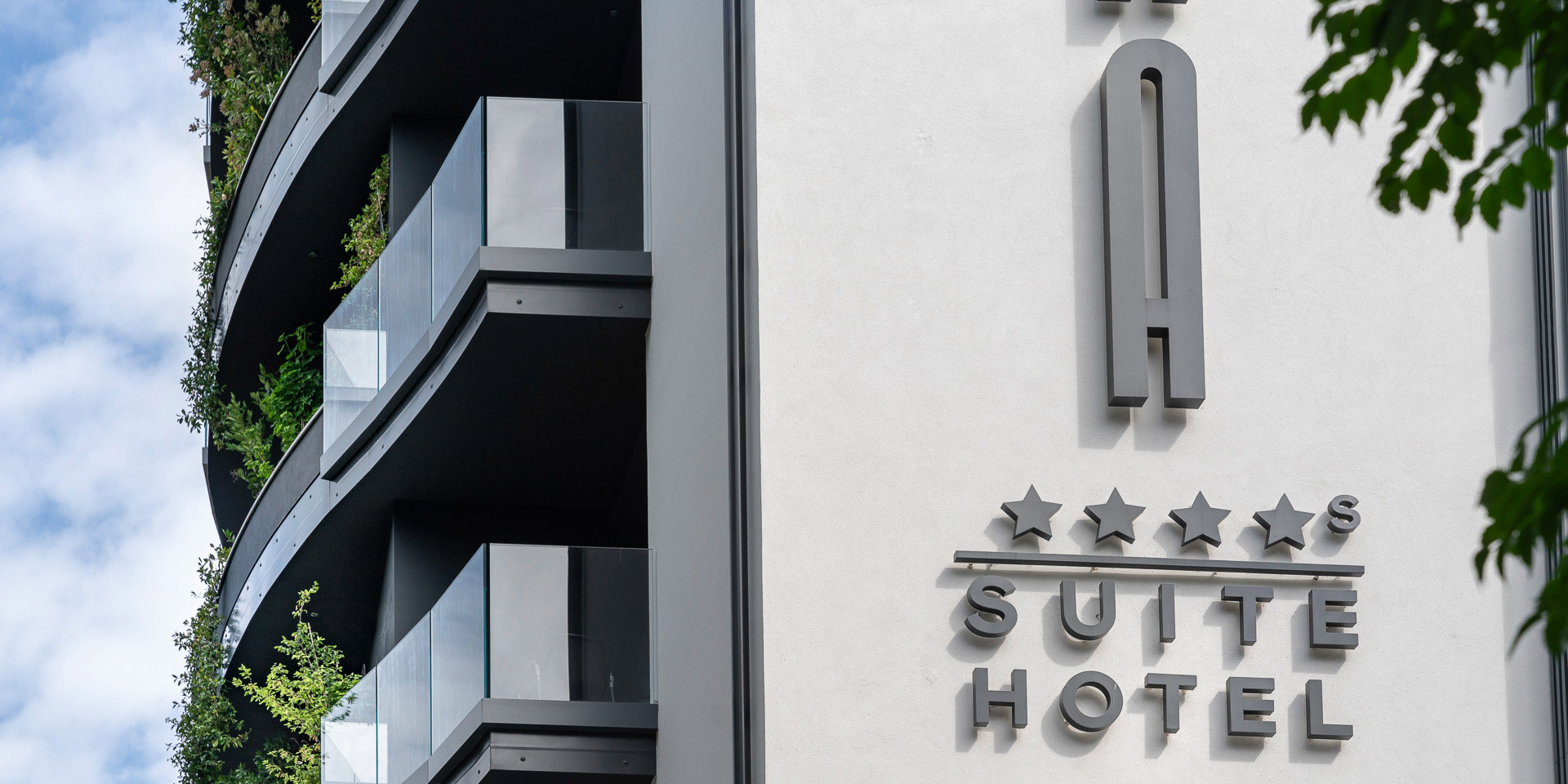 Hotel moderno con balconi verdi, cielo azzurro e insegna a cinque stelle.