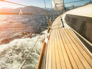 Barca a vela naviga su acque mosse con montagne sullo sfondo al tramonto.