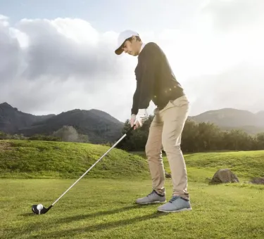 Giocatore di golf in posa per un colpo su un campo verde.