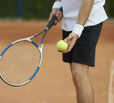 Giocatore di tennis prepara il servizio su un campo in terra rossa.
