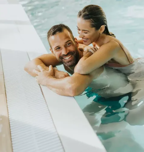 Coppia felice abbracciata in piscina, sorridendo e godendo il momento.