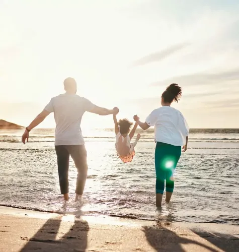 Famiglia felice gioca sulla spiaggia al tramonto, sollevando il bambino tra le onde.