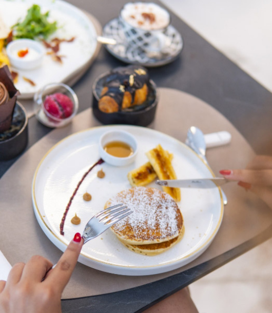 Colazione elegante: pancake soffici, banane, sciroppo, e dolci raffinati su un tavolo accogliente.