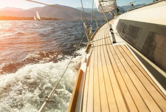 Navigazione a vela con vista monti e mare mosso al tramonto.