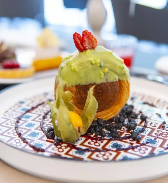 Dolce con glassa verde, fragole e frutta esotica su piatto decorato.