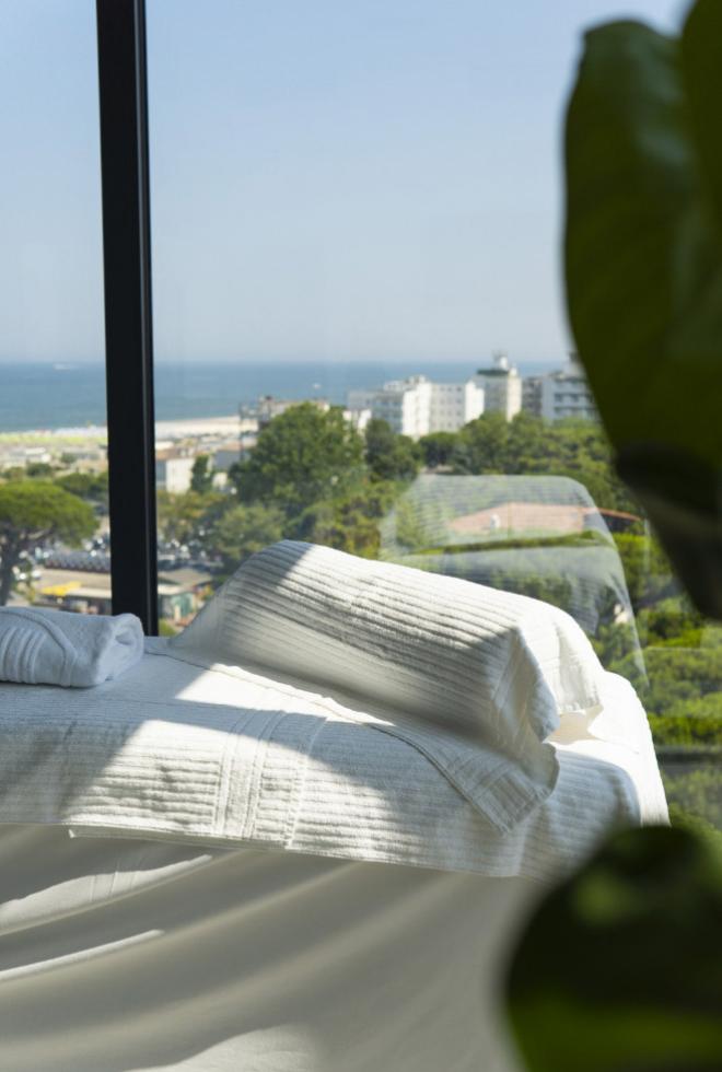 Letto bianco vicino a finestra, vista mare e città, atmosfera rilassante e luminosa.