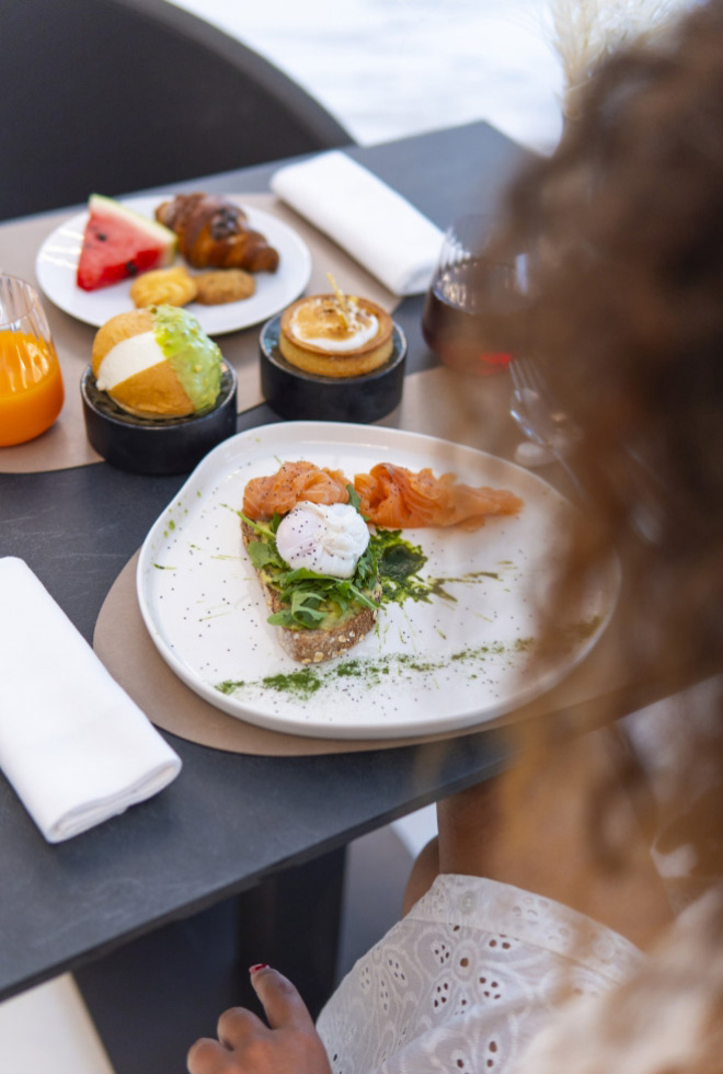 Colazione raffinata con salmone, avocado, dolci e frutta, su tavola elegante.