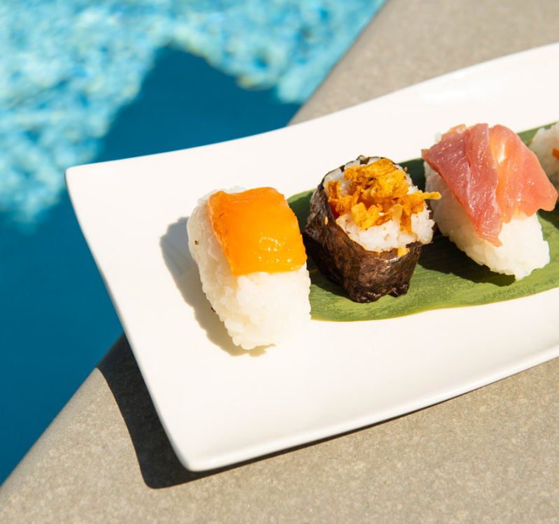 Sushi variopinto su piatto bianco, a bordo piscina, evoca freschezza e relax estivo.