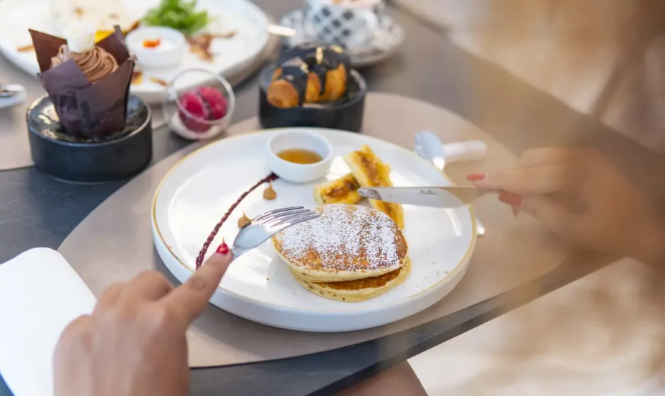Pancakes con zucchero a velo e sciroppo, accompagnati da dolci e frutta.