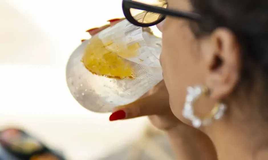 Donna con occhiali beve da un bicchiere con ghiaccio e fetta d'arancia.