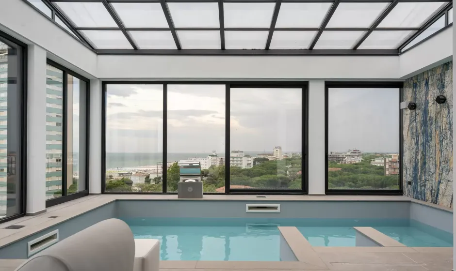 Piscina interna con vista panoramica sul mare e città attraverso grandi finestre.