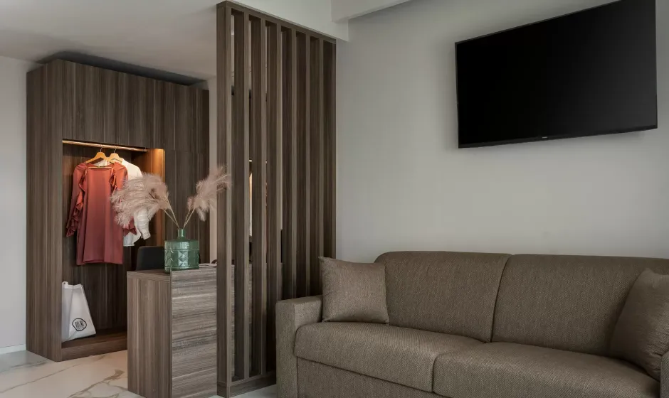 Stanza moderna con divano, TV a parete e armadio aperto con abiti appesi.