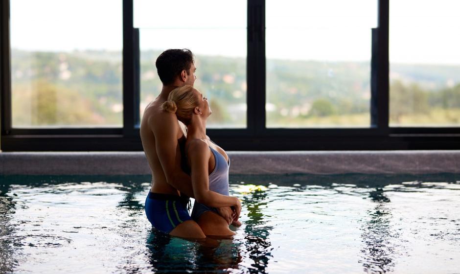 Coppia abbracciata in piscina con vista panoramica dalla finestra.
