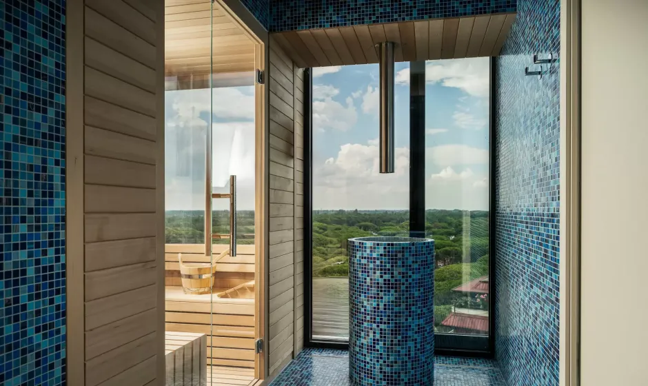 Sauna moderna con vista panoramica, rivestimenti in legno e mosaico blu.