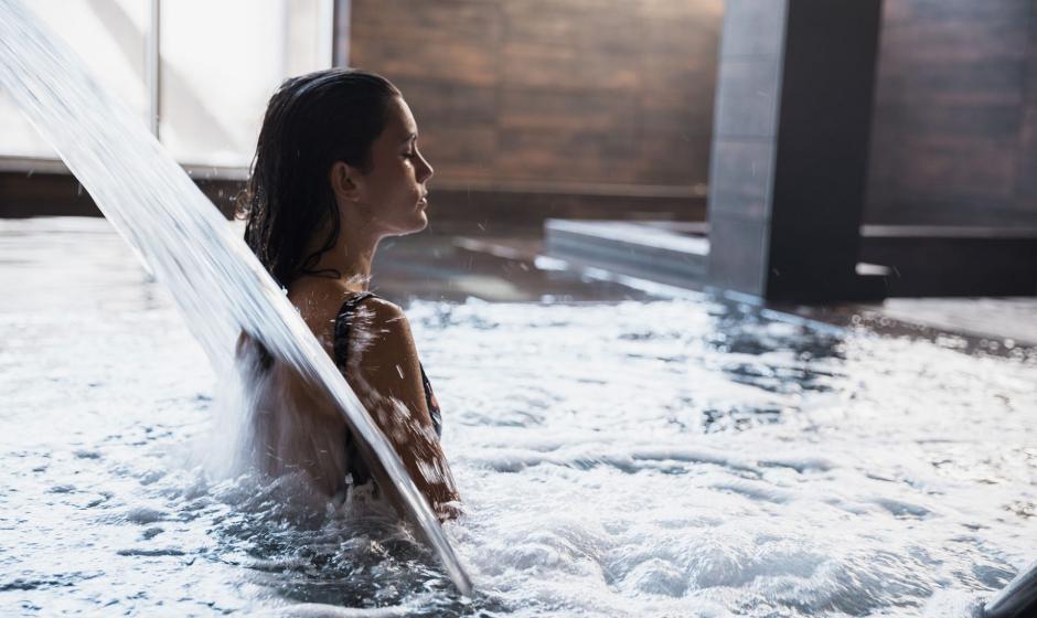 Donna rilassata in una piscina con cascata d'acqua in un ambiente interno.
