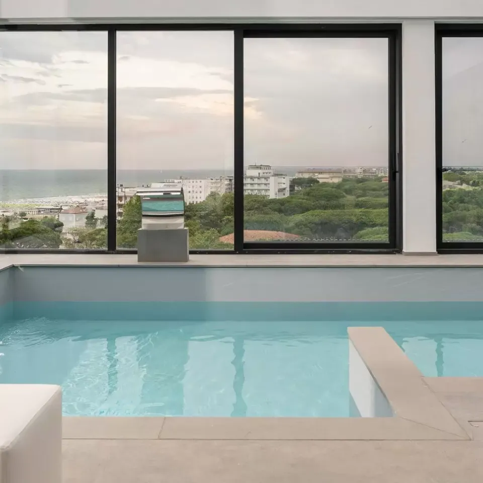 Piscina interna con vista panoramica sul mare e città attraverso ampie finestre.