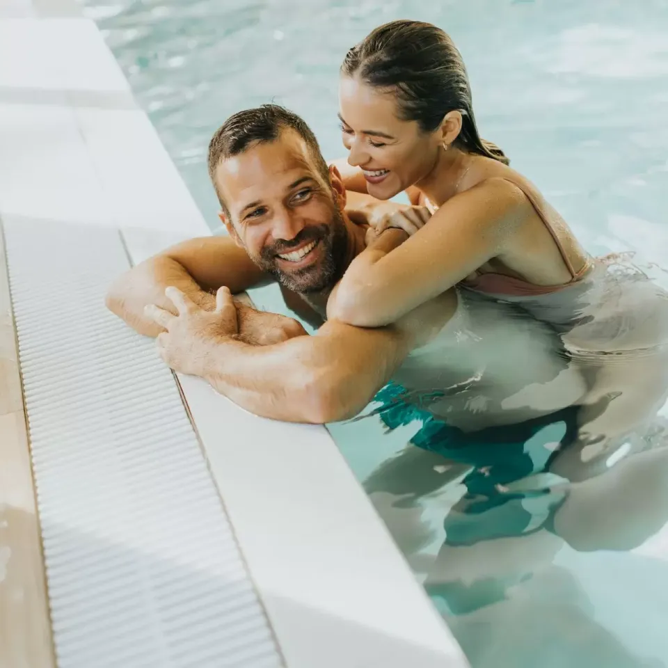 Coppia felice in piscina, abbracciati e sorridenti, godendo un momento di relax acquatico.