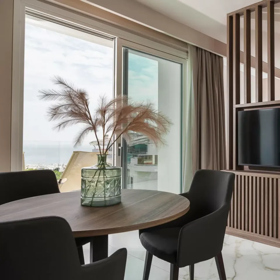 Camera moderna con divisorio in legno, TV, tavolo e vista sul mare.