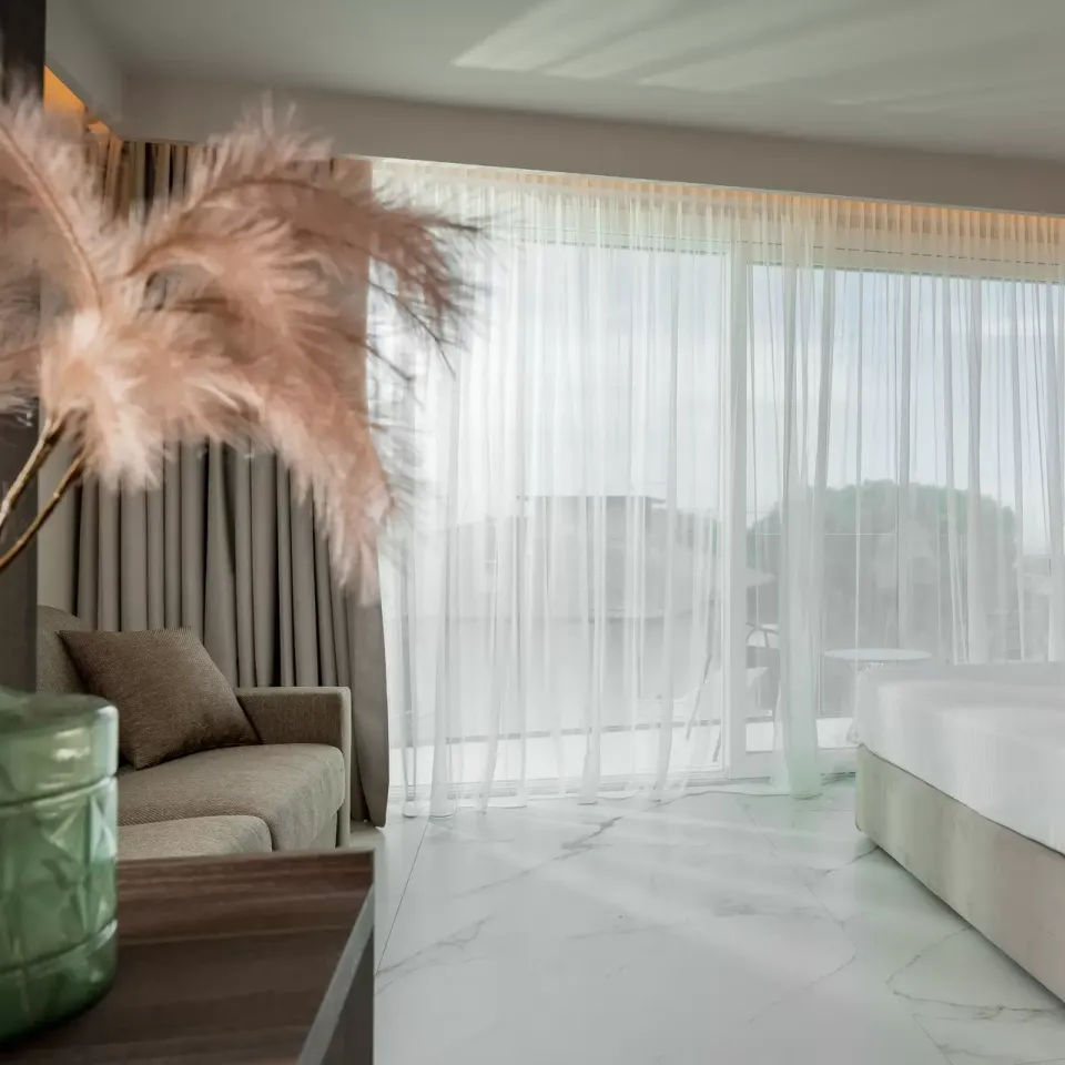 Camera moderna con letto, divano e ampie finestre, decorata con piante ornamentali.