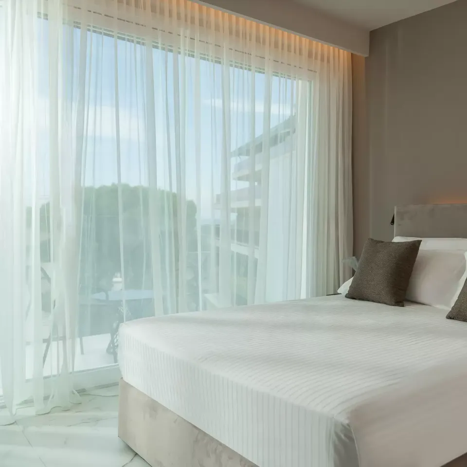 Camera moderna con letto matrimoniale, tende trasparenti e luce naturale.