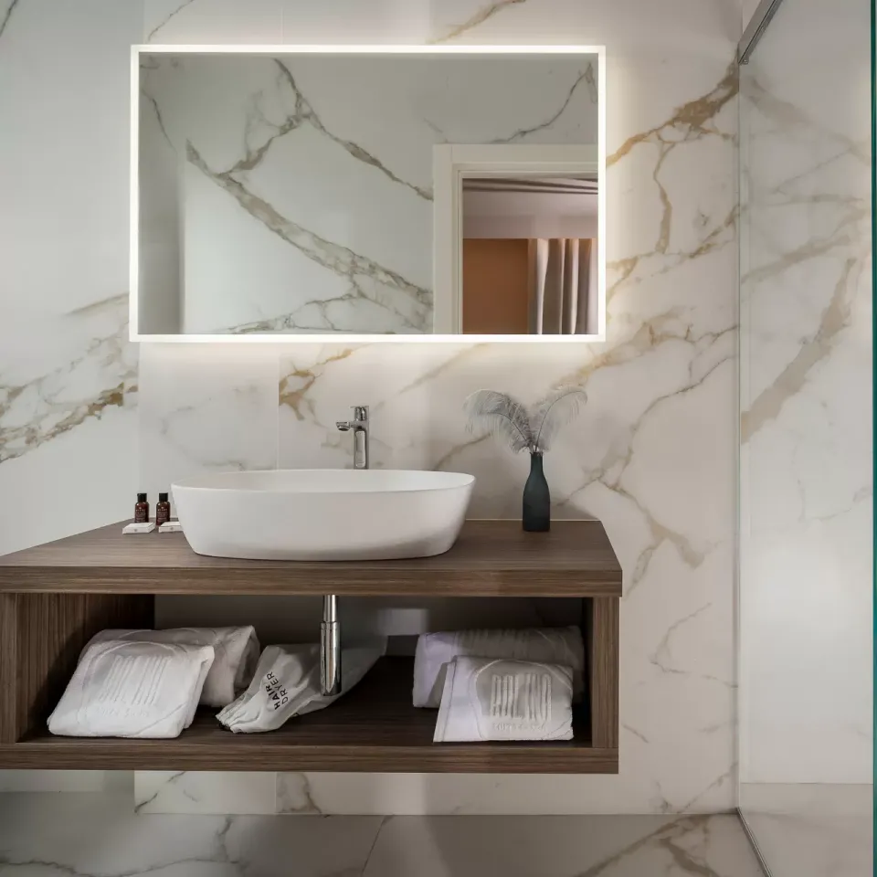 Elegante bagno moderno con lavabo sospeso, specchio illuminato e doccia in vetro.